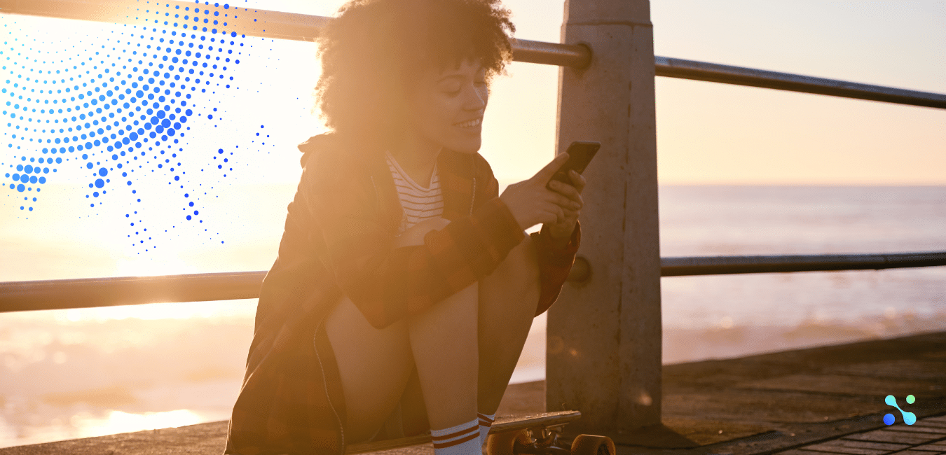 Young woman using a smartphone by the seaside at sunset, symbolizing the emerging potential of blockchain technology.
